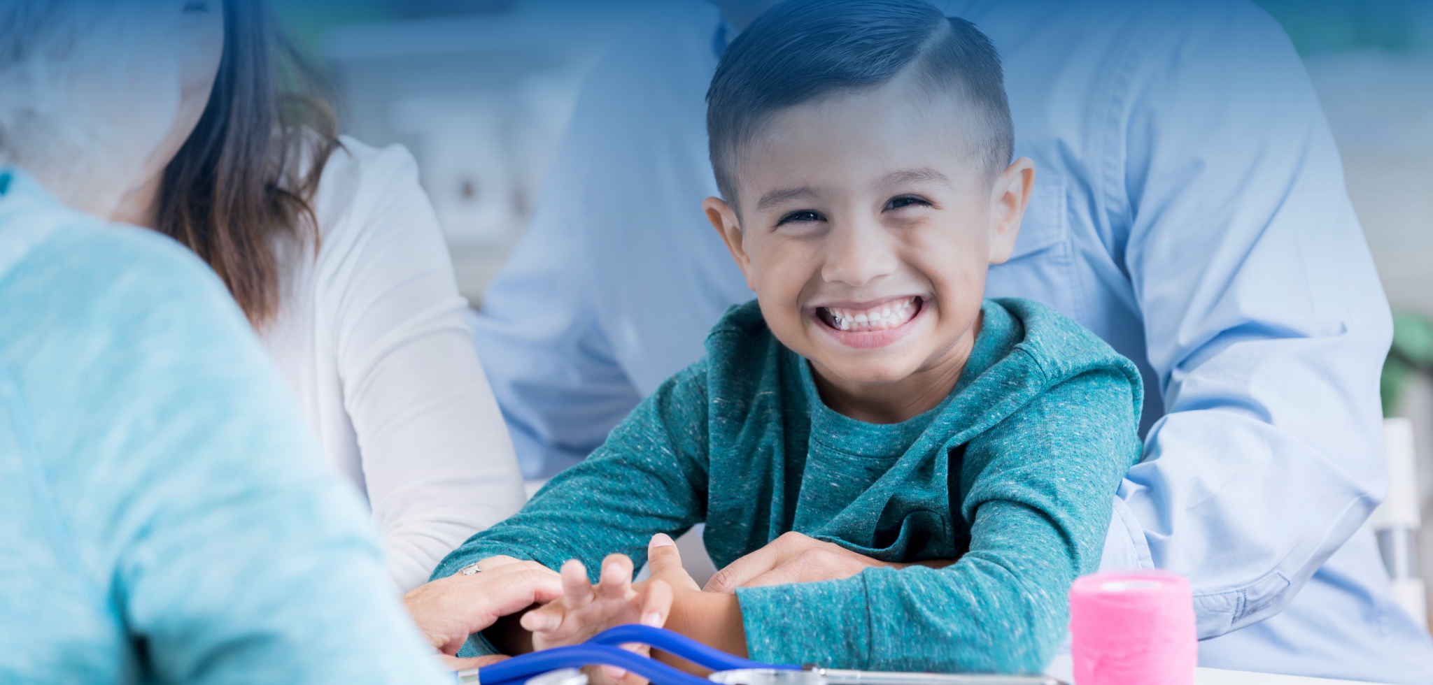 United Way health services, young boy smiling at the camera, child sitting at a doctors office with his parents, nurse speaking with child's parents